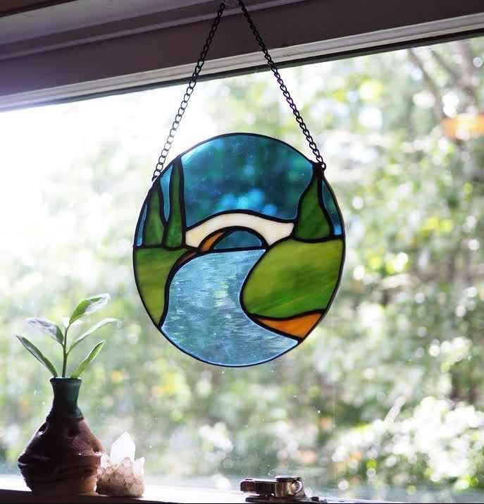 A circular stained glass piece with a river and a bridge going over it
